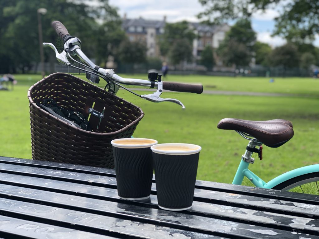 Two cups of coffee on a table in front of a mint coloured Dutch bike.