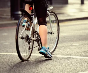 Cyclist waiting to cross road in rain and sun.